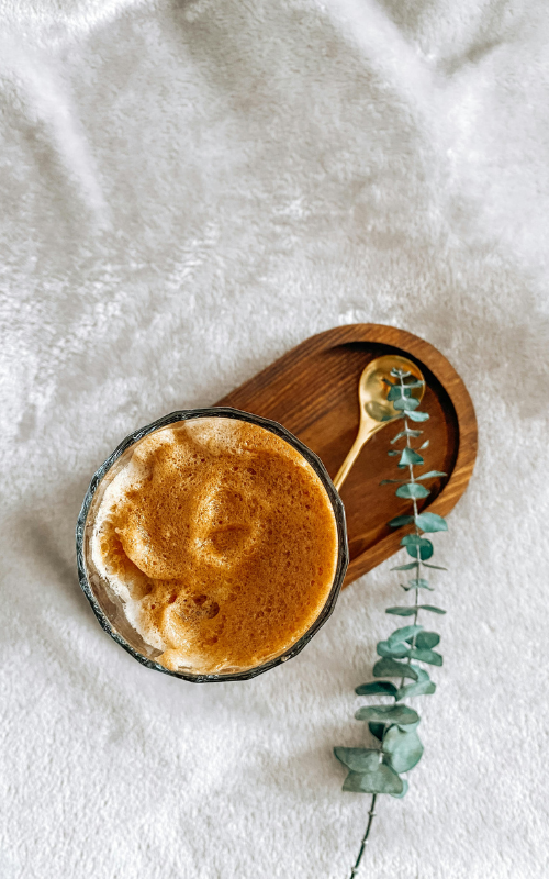 Cappuccino in a glass with wooden coaster and eucalyptus leaf on white fabric background